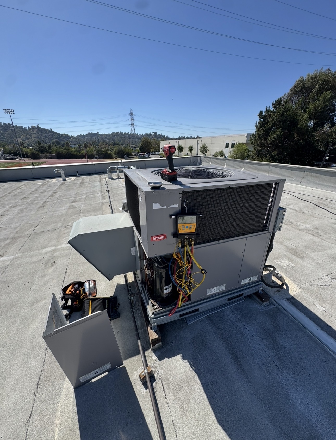 HVAC technician servicing a rooftop air-conditioning unit with diagnostic gauges