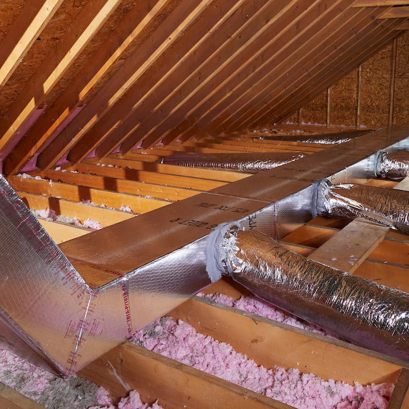 Insulated HVAC ductwork running through a residential attic with exposed rafters