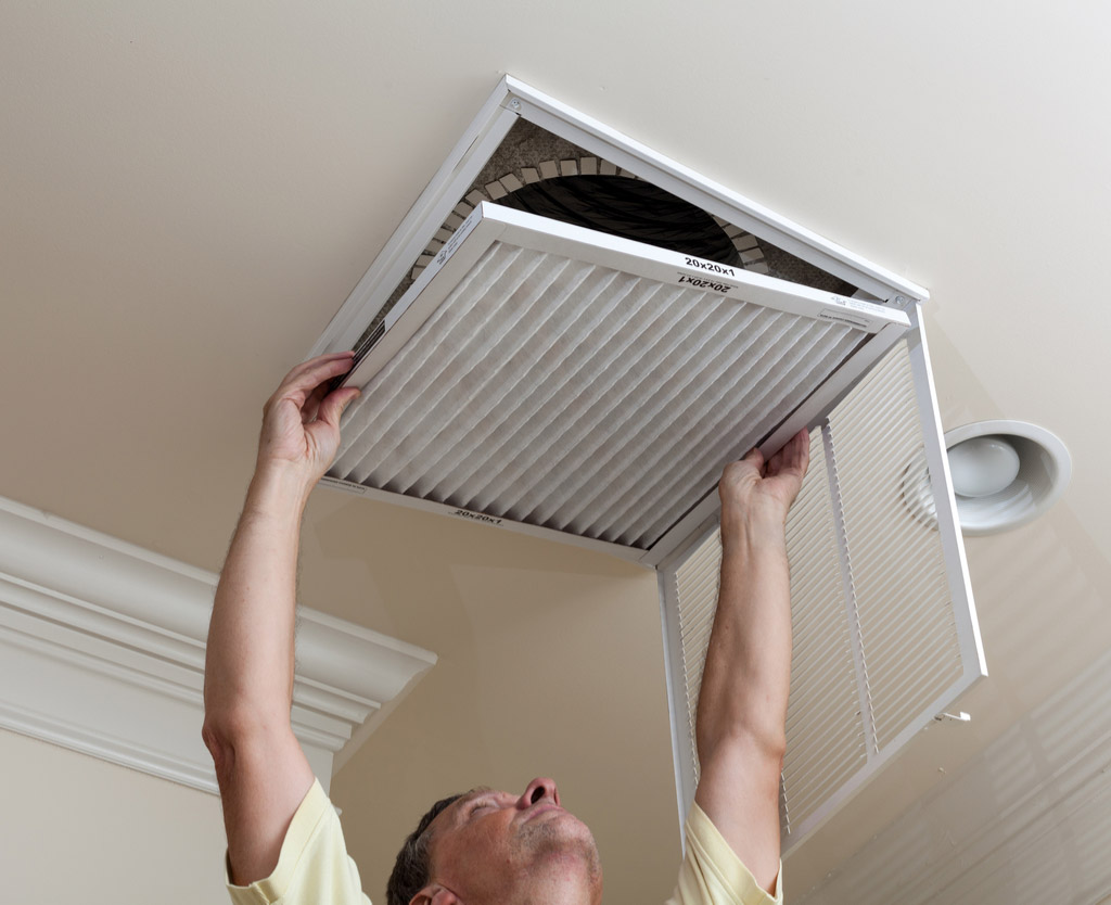 Homeowner replacing a pleated HVAC air filter in a ceiling return vent